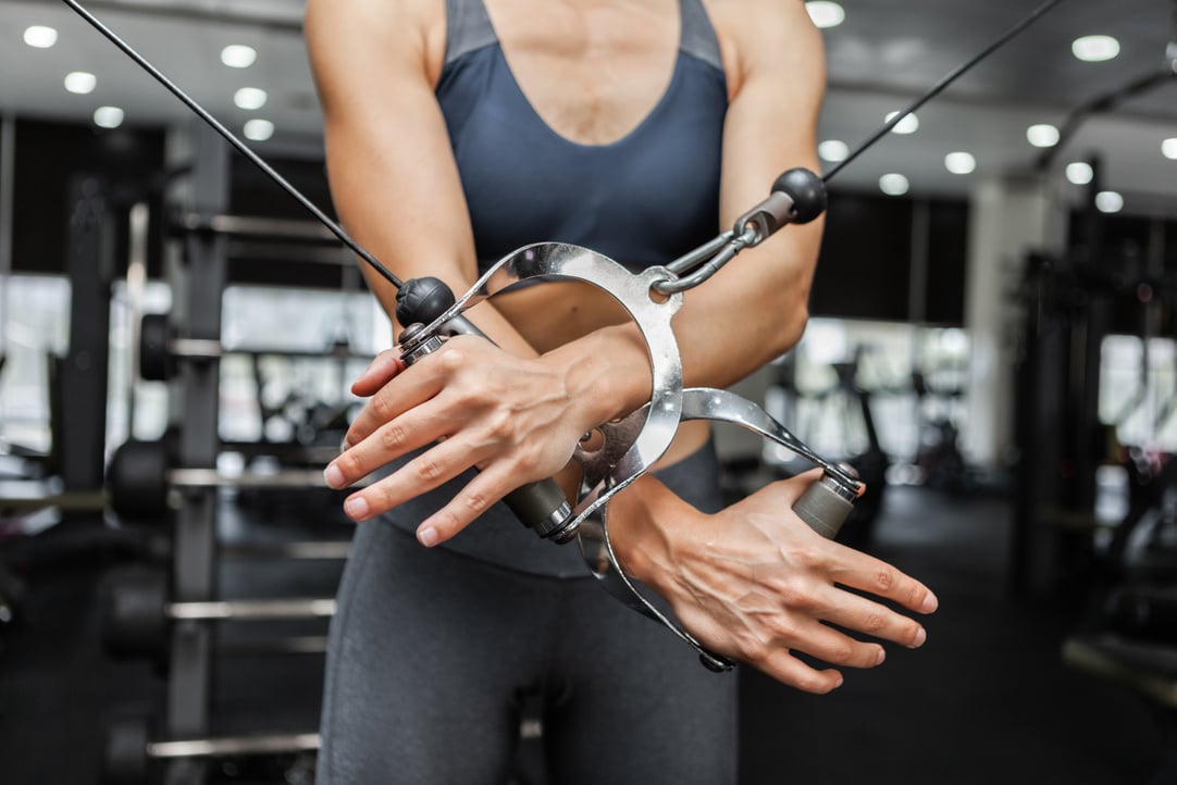 Athletic woman exercising muscles in crossover cable exercise machine in modern gym